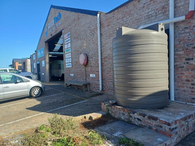 Industrial property exterior featuring exposed brickwork, a large water storage tank, and paved driveway access to the main workshop area.