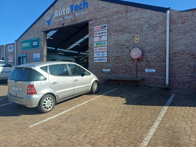 Front exterior view of an industrial workshop featuring exposed brickwork, signage, and a paved parking area with an industrial roller door entrance.