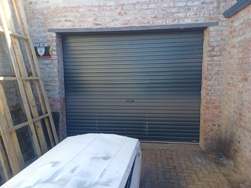 A secure industrial-style garage featuring a dark grey roller shutter door set within an exposed brick facade and paved exterior area.