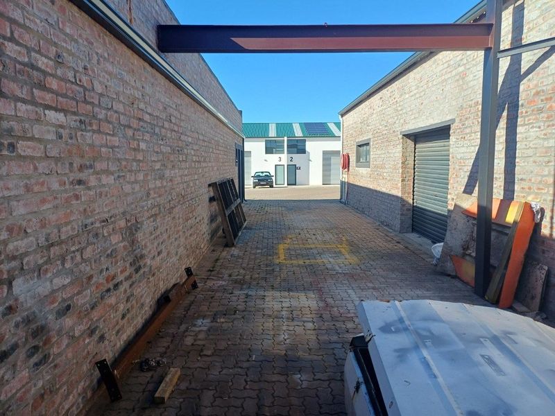 An industrial rear access lane featuring exposed brick walls, a steel I-beam structure, and a roller shutter door for loading access.