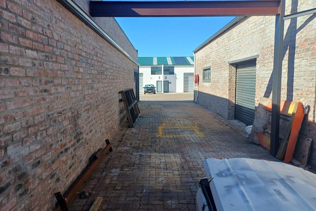 An industrial rear access lane featuring exposed brick walls, a steel I-beam structure, and a roller shutter door for loading access.