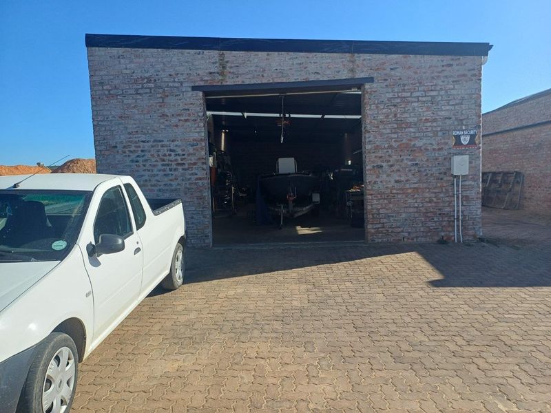 Industrial garage unit featuring exposed brick construction and a paved driveway, suitable for storage or workshop use.