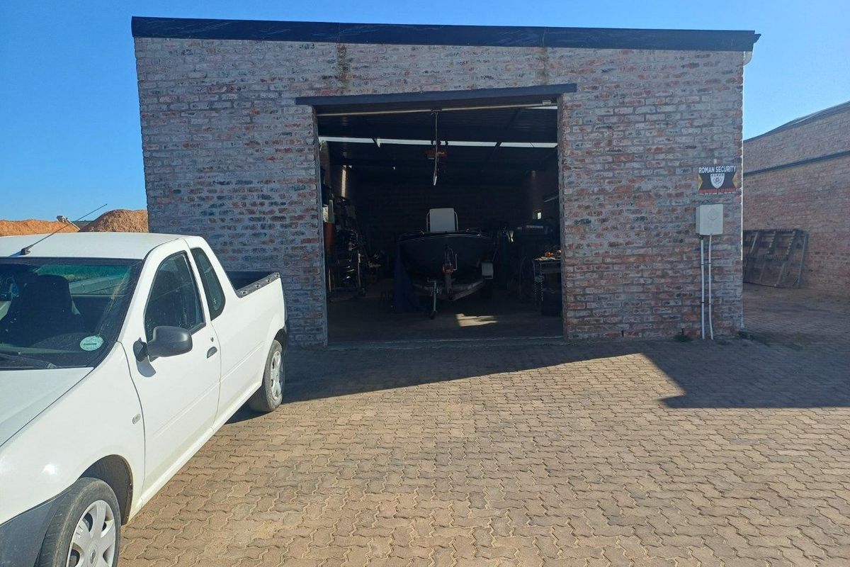 Industrial garage unit featuring exposed brick construction and a paved driveway, suitable for storage or workshop use.