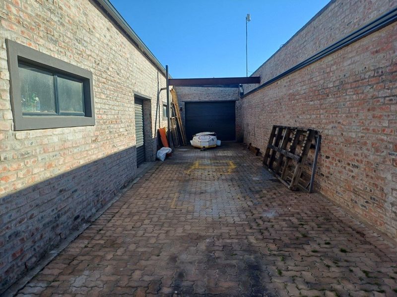 A secure industrial rear yard featuring exposed brick walls, paved flooring, and a roller shutter door access point.