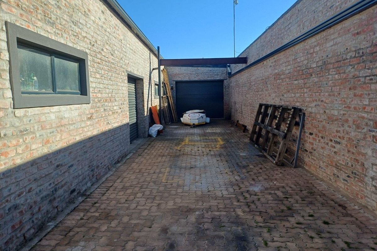 A secure industrial rear yard featuring exposed brick walls, paved flooring, and a roller shutter door access point.