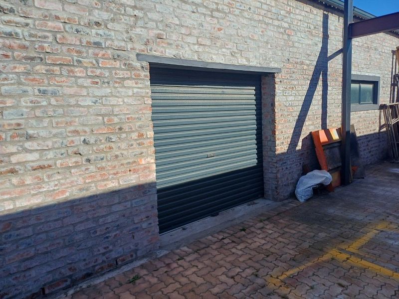 Exterior view of an industrial building featuring exposed brick walls and a secure roller shutter door access point.