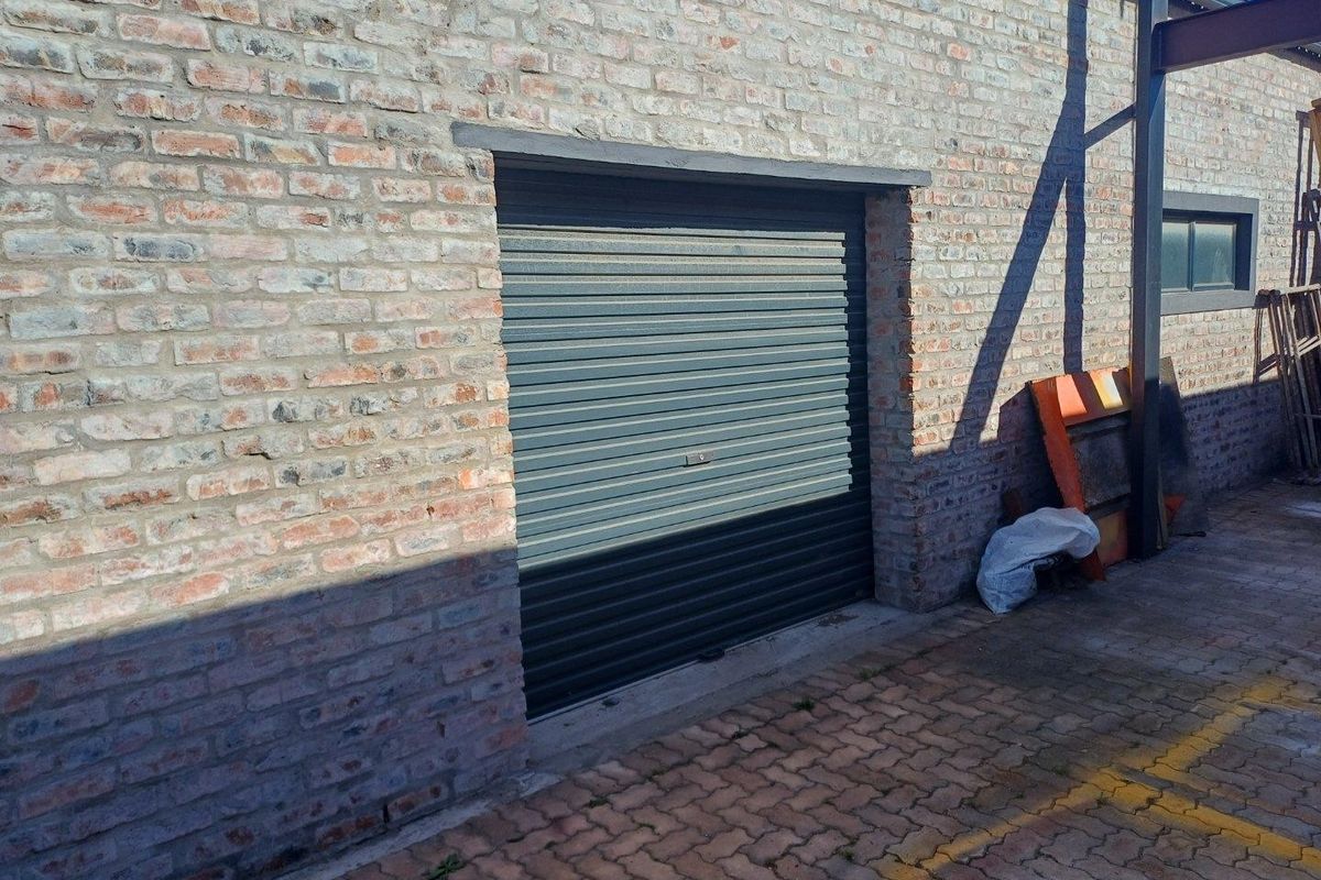 Exterior view of an industrial building featuring exposed brick walls and a secure roller shutter door access point.