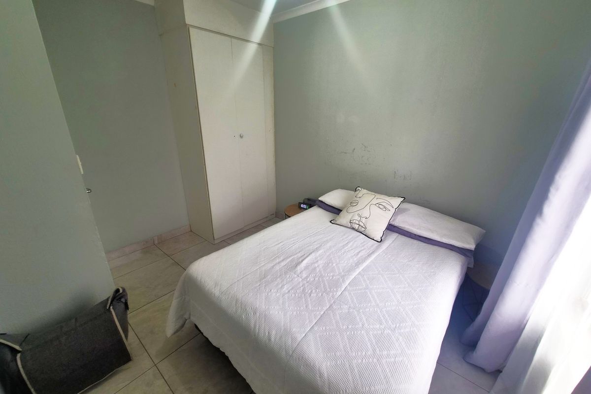 A functional bedroom featuring tiled flooring, a built-in wardrobe, and neutral wall finishes, offering a clean and simple living space.
