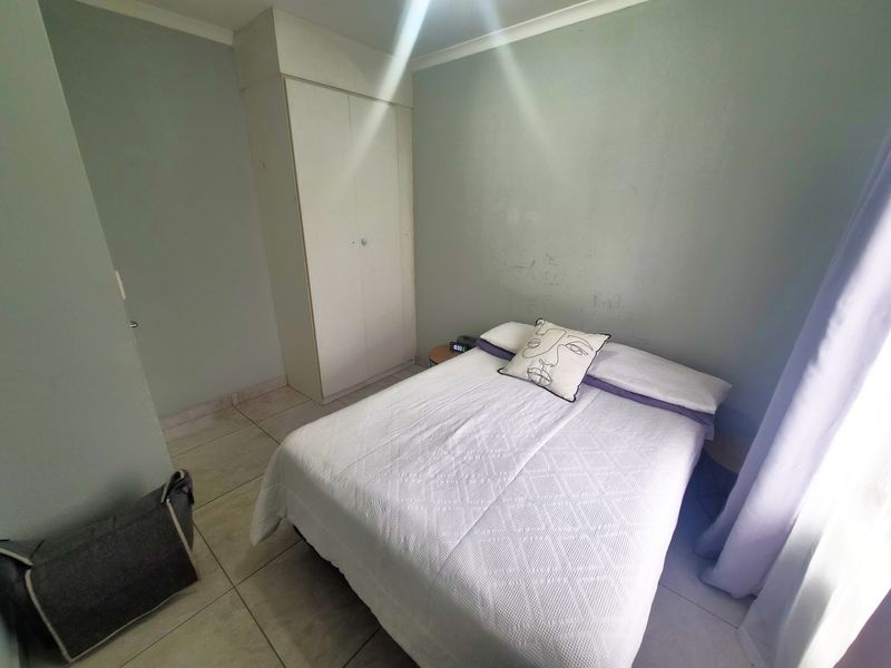 A functional bedroom featuring tiled flooring, a built-in wardrobe, and neutral wall finishes, offering a clean and simple living space.