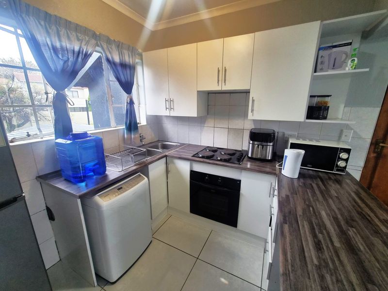 Compact kitchen featuring white cabinetry, dark laminate countertops, built-in oven and hob, and tiled flooring with a functional layout.