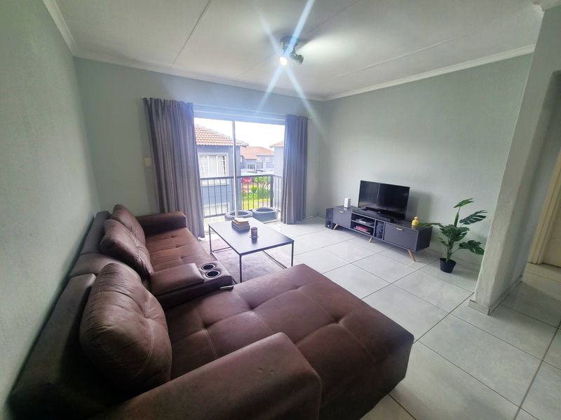 A bright living room featuring large format floor tiles and a sliding glass door providing access to a balcony.
