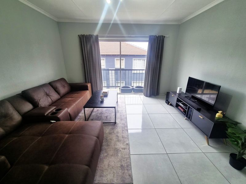 A well-maintained living room featuring large format floor tiles, coved ceilings, and a sliding glass door providing access to a balcony.