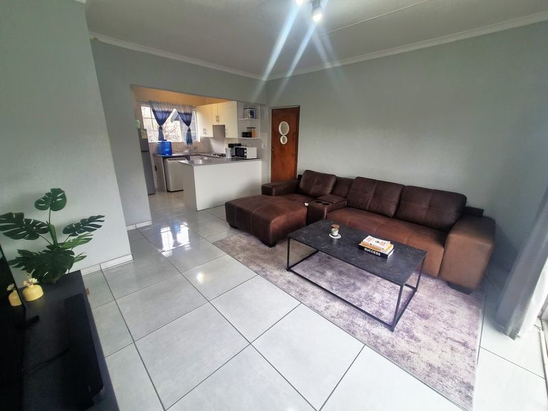 Open-plan living area featuring tiled floors and a connected kitchen with built-in cabinetry and appliances.