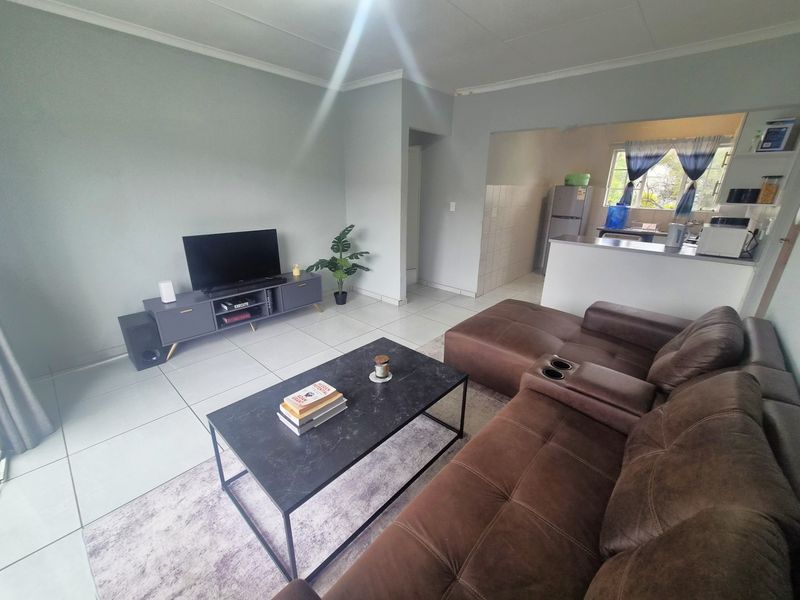 Open plan living area featuring tiled flooring and a functional kitchen with a breakfast bar, creating a seamless flow between spaces.