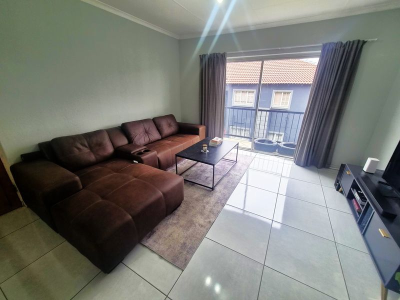 A bright living room featuring large format floor tiles and a sliding glass door providing access to a balcony.