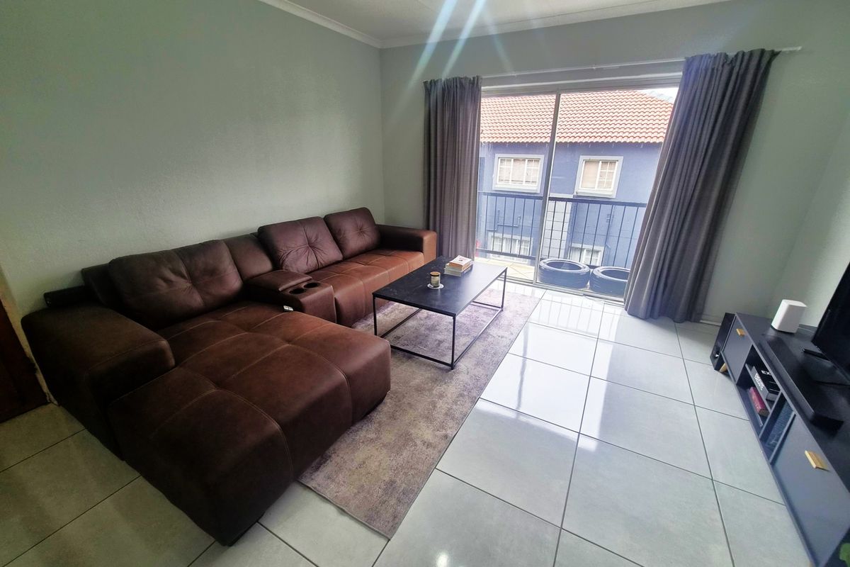 A bright living room featuring large format floor tiles and a sliding glass door providing access to a balcony.