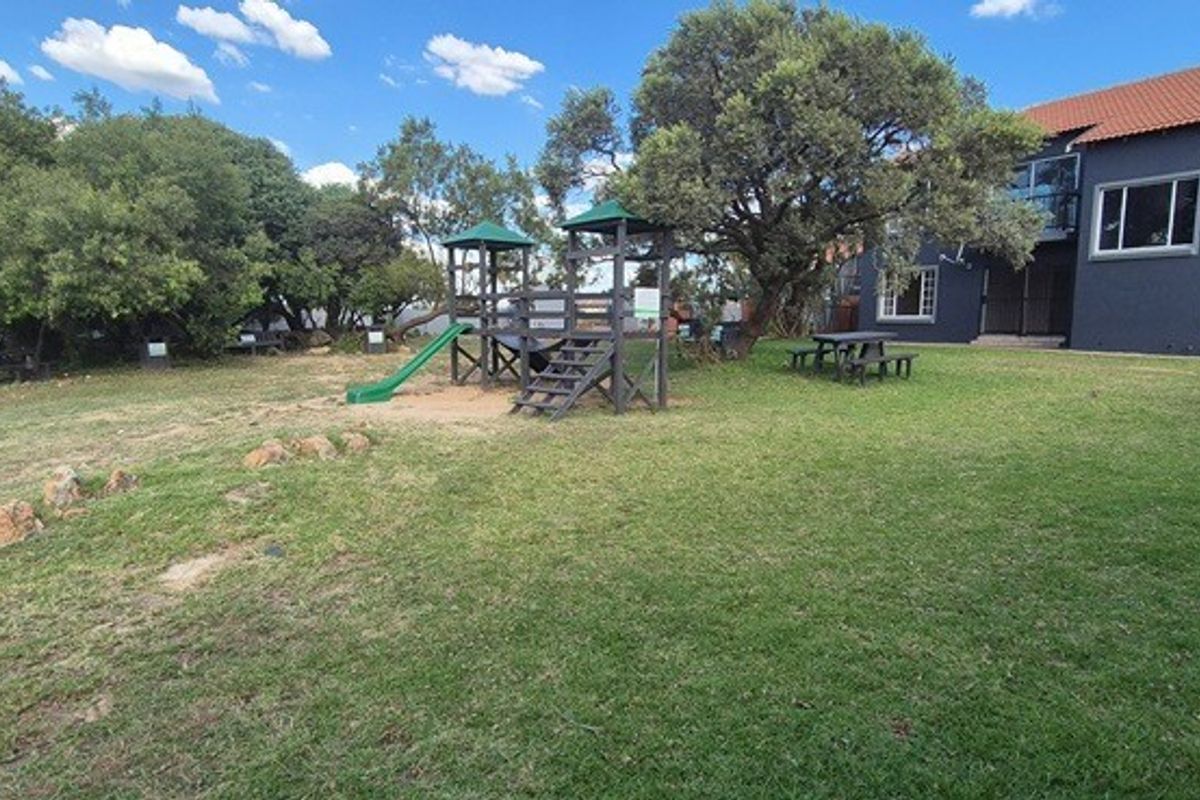 A spacious rear garden area featuring a lawn, mature trees, and a view of the apartment building's rear facade with balconies.