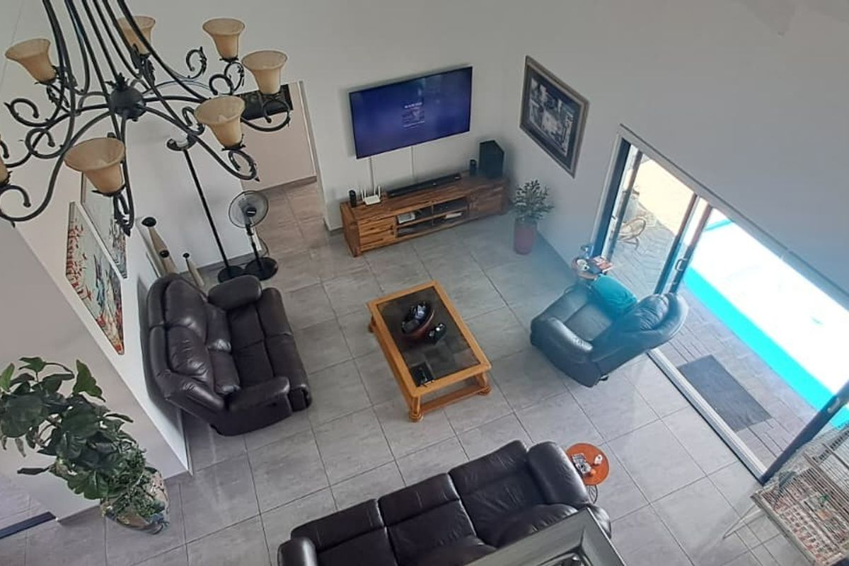 Spacious living room with high vaulted ceilings, large tiled floors, and sliding glass doors providing direct access to the outdoor pool area.