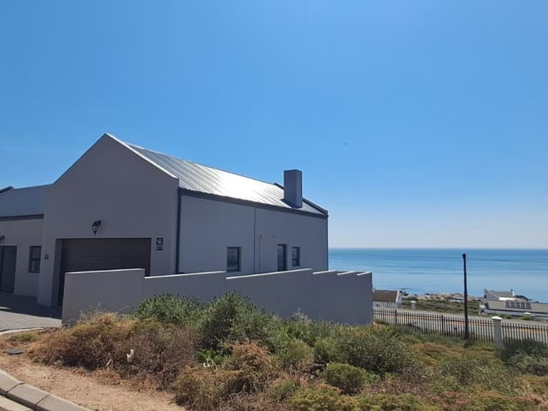 A modern coastal home featuring a metal roof, paved driveway, and garage, set against a scenic ocean view.