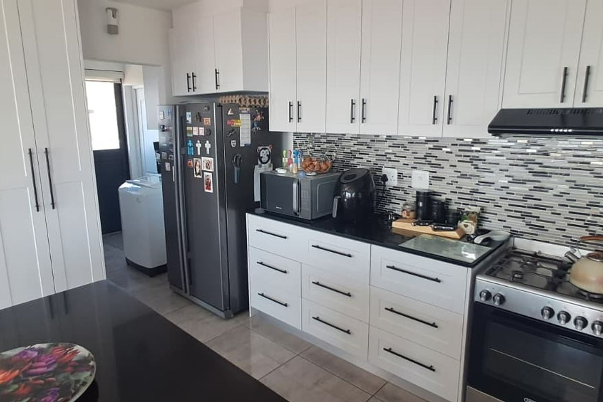 Modern kitchen featuring white cabinetry, black granite countertops, a mosaic tile backsplash, and a gas stove with an integrated extractor fan.