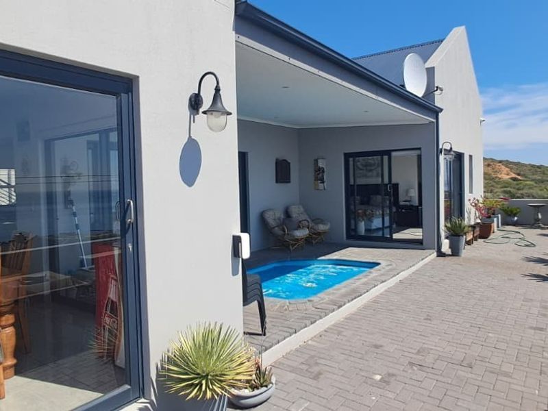 A paved outdoor patio area featuring a built-in plunge pool, sliding glass door access to the interior, and coastal views.