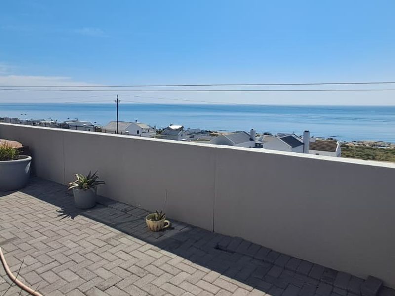 An elevated outdoor patio area featuring paved flooring and a solid parapet wall, offering expansive coastal and ocean views.