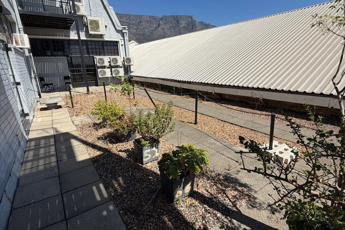 An outdoor rear area featuring a paved walkway, gravel landscaping, and multiple wall-mounted air conditioning units against a metal-roofed office building.