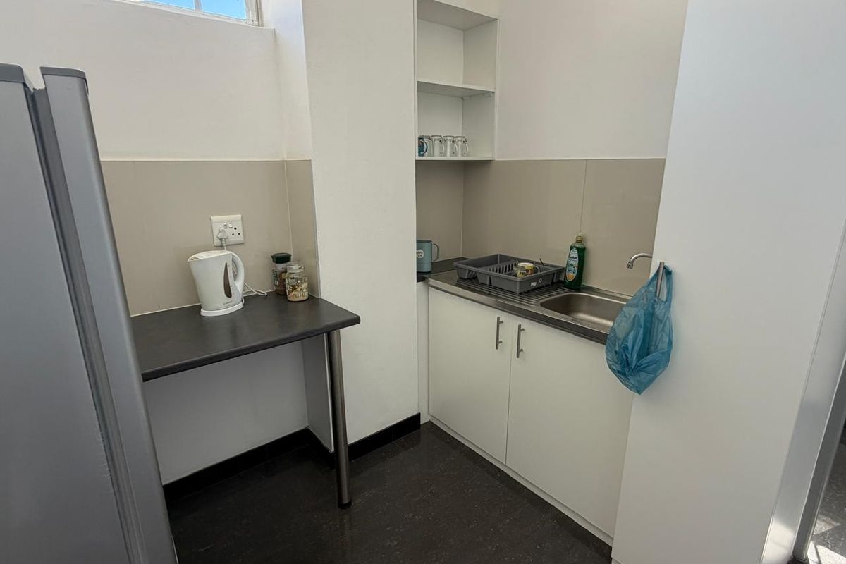 A compact office kitchenette featuring white cabinetry, a stainless steel sink, laminate countertop, and tiled splashback.