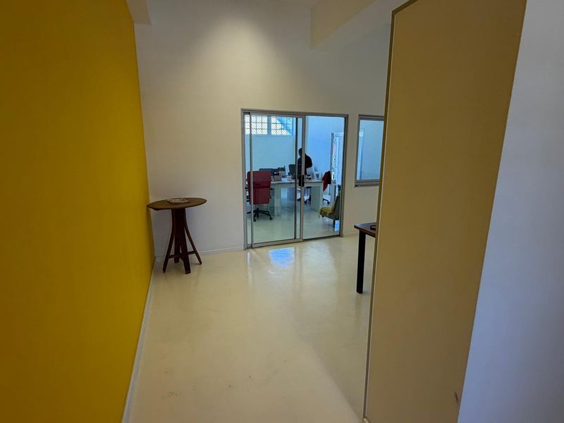 A bright, open-plan office space featuring polished epoxy flooring, a vibrant yellow accent wall, and a sliding glass door leading to an adjacent workspace.