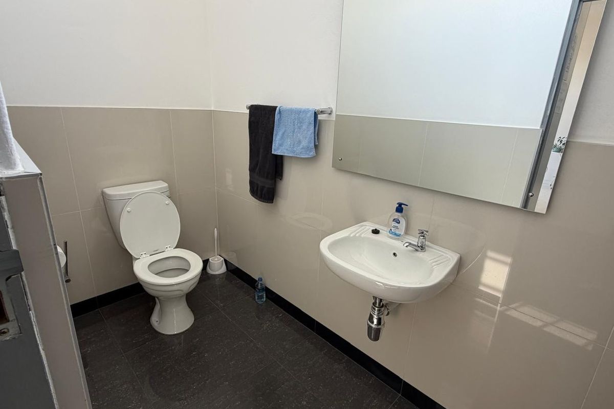 A clean, functional office bathroom featuring a wall-mounted basin, toilet, large mirror, and neutral tiled finishes.
