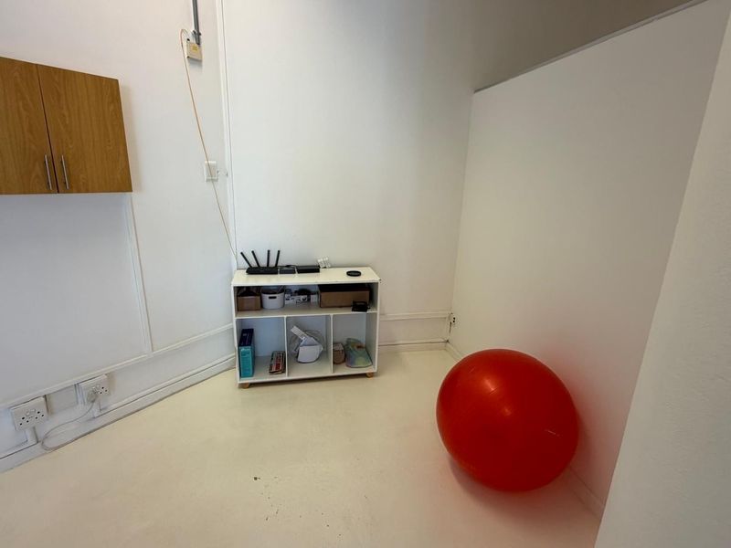 A compact office space featuring white walls, surface-mounted electrical conduit, and wall-mounted storage cabinetry.