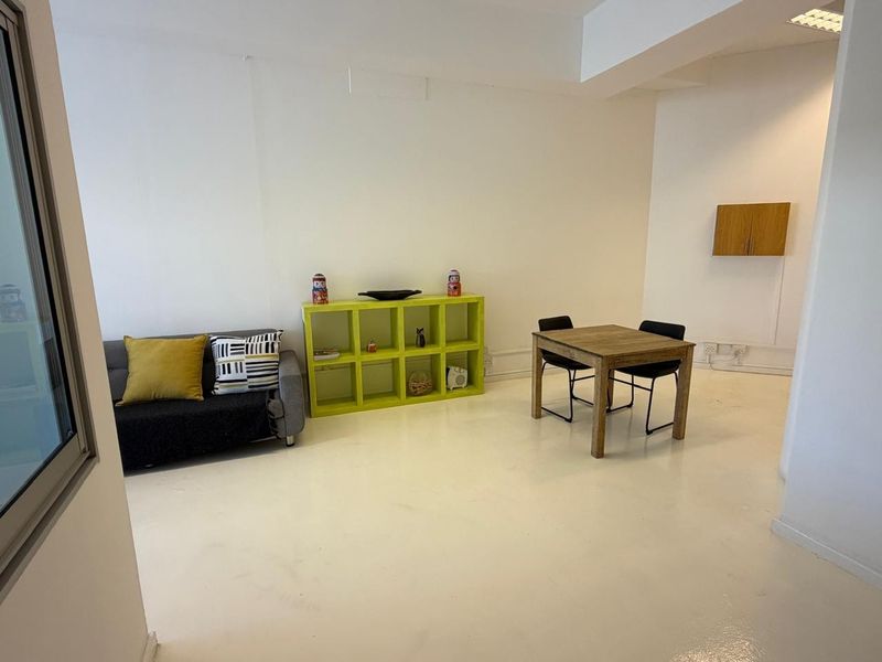 A bright, open-plan office space featuring white flooring, recessed lighting, and a wall-mounted storage cabinet, providing a versatile workspace environment.
