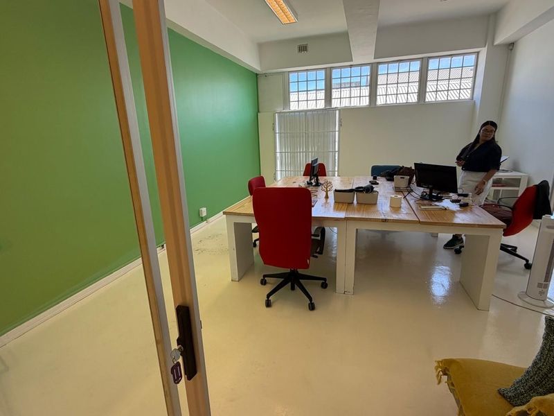 A bright office space featuring high ceilings, large multi-pane windows, and a vibrant green accent wall with durable epoxy flooring.