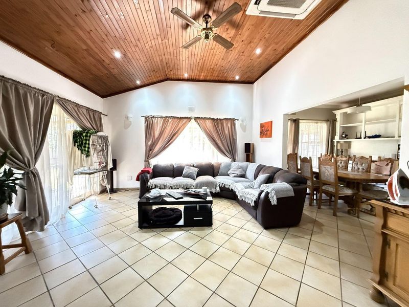 Spacious open-plan living and dining area featuring a vaulted timber ceiling, tiled flooring, and integrated shelving, offering a bright and functional layout.