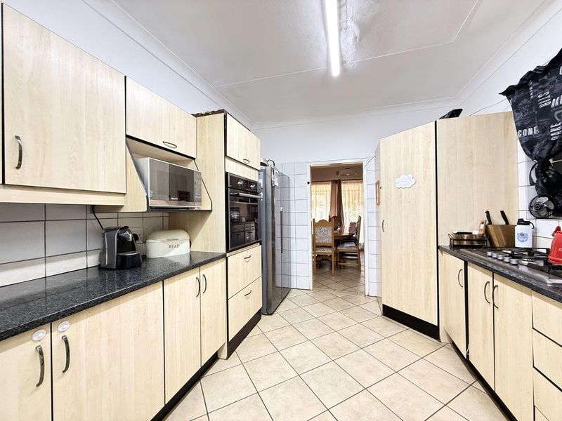 A functional kitchen featuring light wood-finish cabinetry, dark laminate countertops, built-in oven and microwave, gas hob, and tiled flooring.