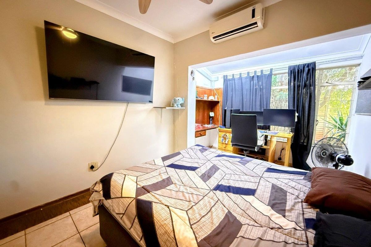 A bedroom featuring tiled flooring, a ceiling fan, a wall-mounted air conditioning unit, and a built-in study nook area.