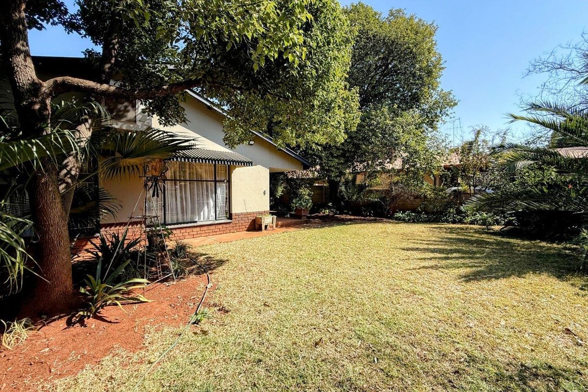 A view of the rear garden featuring a paved patio area, mature trees, and a well-maintained lawn adjacent to the house facade.