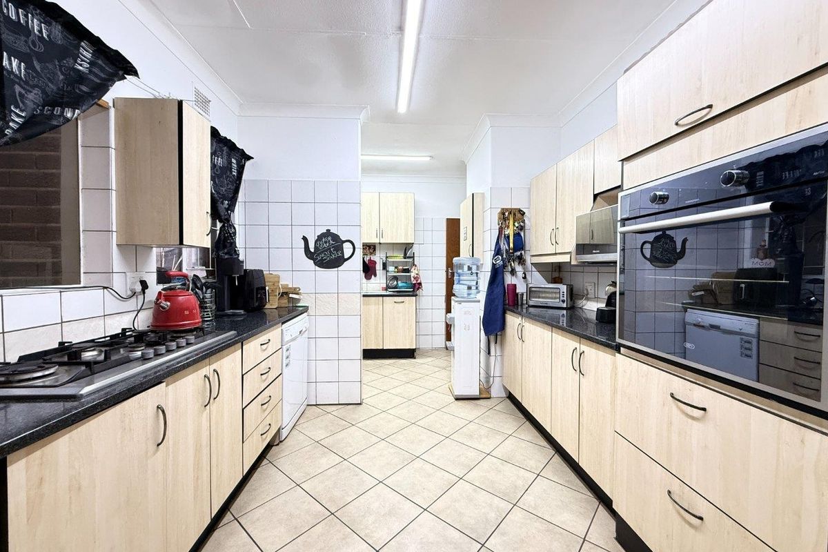 A functional galley-style kitchen featuring light wood-finish cabinetry, dark countertops, a gas hob, and a built-in oven with tiled flooring throughout.