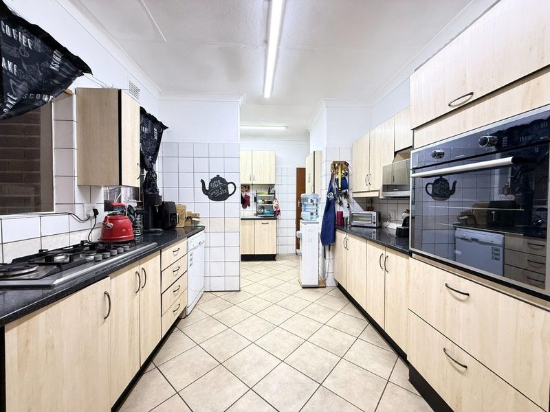 A functional galley-style kitchen featuring light wood-finish cabinetry, dark countertops, a gas hob, and a built-in oven with tiled flooring throughout.