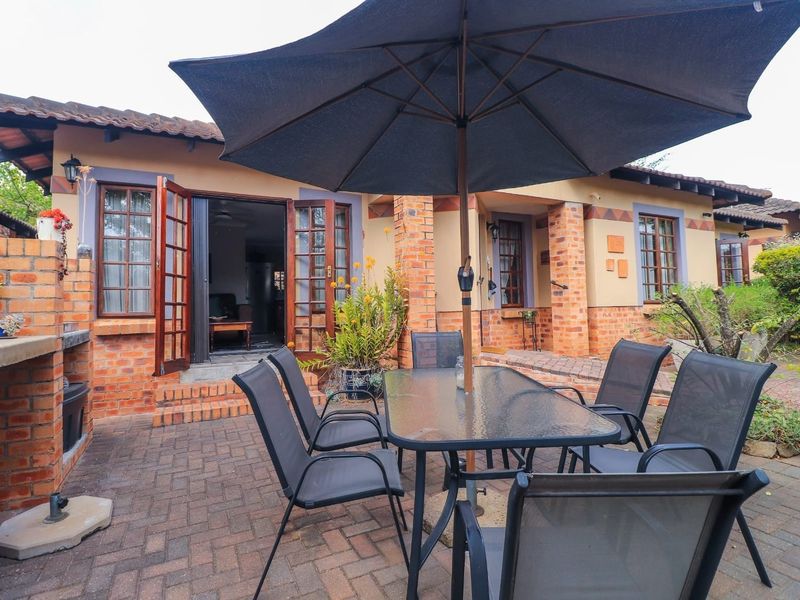 A charming rear patio featuring brick paving, a built-in brick braai, and direct access to the interior through timber-framed french doors.