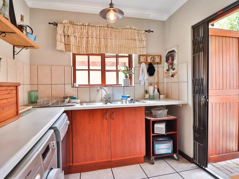 A functional laundry area featuring built-in cabinetry, a double sink, tiled backsplash, and direct access to the exterior through a timber door.