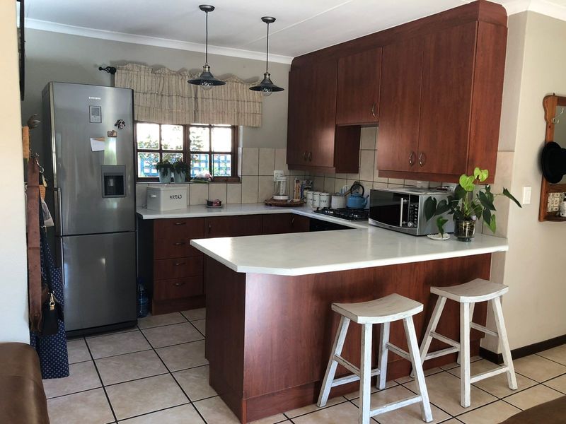 A functional kitchen featuring dark wood cabinetry, white laminate countertops, tiled flooring, and a breakfast bar peninsula with pendant lighting.