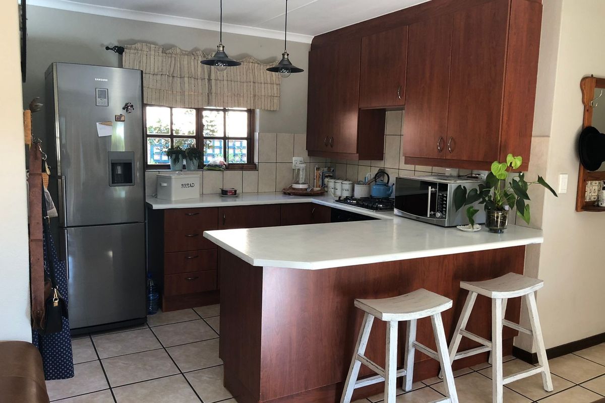 A functional kitchen featuring dark wood cabinetry, white laminate countertops, tiled flooring, and a breakfast bar peninsula with pendant lighting.