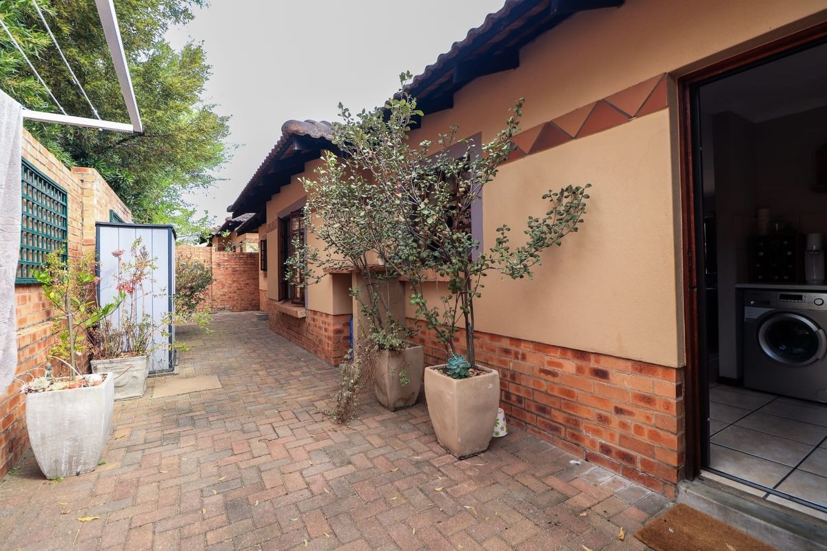 A rear exterior view of the townhouse featuring brick paving, a brick boundary wall, and access to the laundry area.