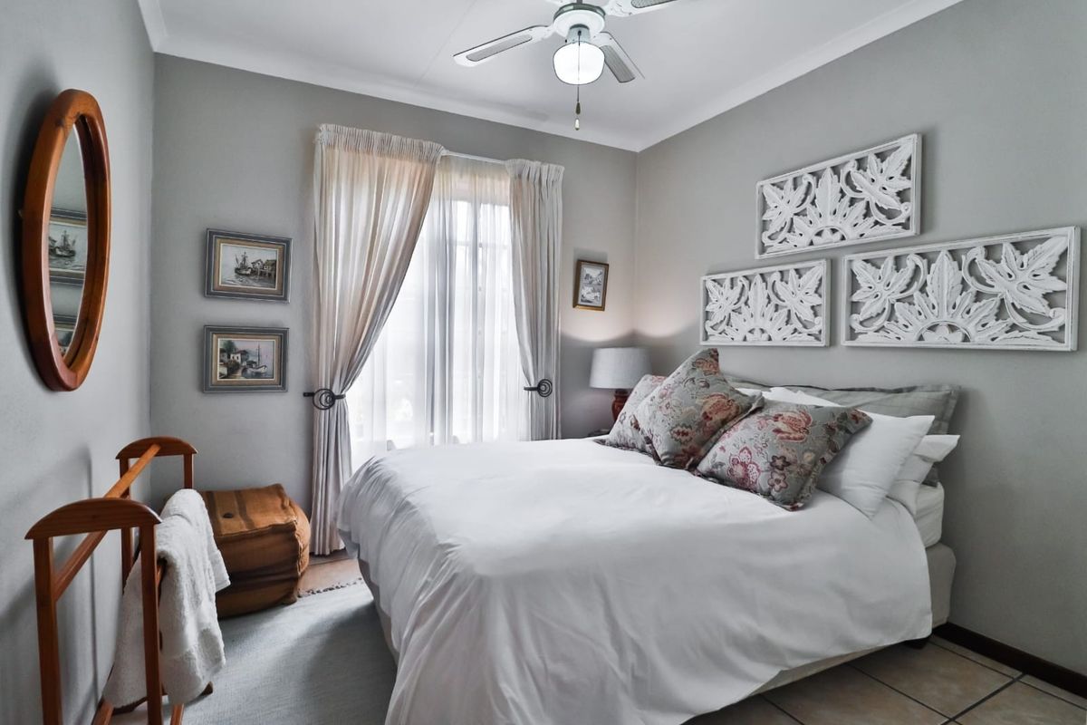 A well-maintained bedroom featuring tiled flooring, a ceiling fan, and large windows with curtain tracks, offering a comfortable and functional living space.