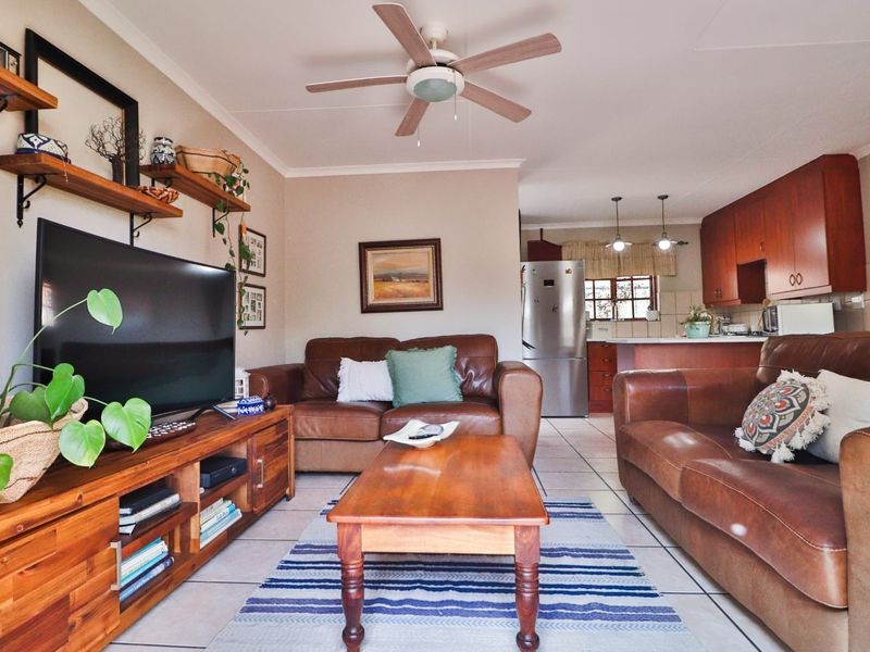 Open-plan living area featuring tiled flooring, a ceiling fan, and a functional kitchen with wooden cabinetry and breakfast counter.