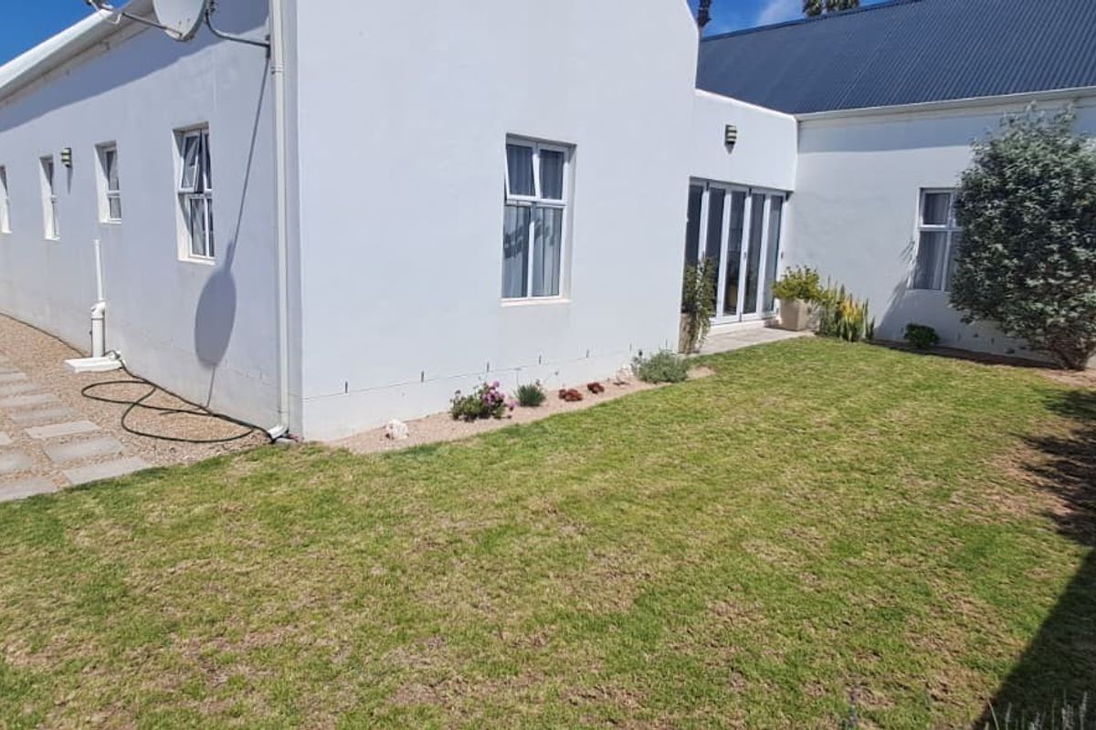 Rear view of the property featuring a well-maintained lawn, paved side walkway, and white exterior walls with sliding glass door access.