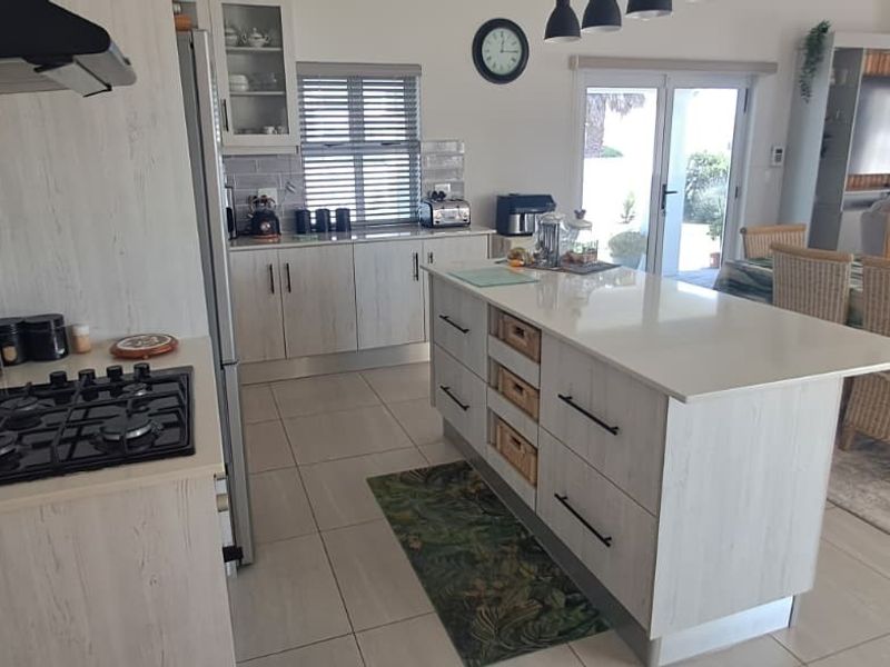 Modern open-plan kitchen featuring a central island with stone countertops, gas hob, extractor fan, and light wood-finish cabinetry, flowing into the dining and living area.