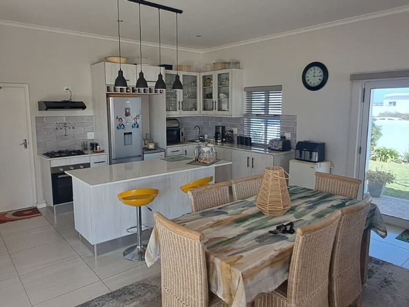 Open-plan kitchen and dining area featuring modern cabinetry, a central island, tiled floors, and direct access to the garden through glass sliding doors.