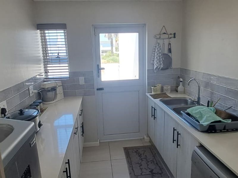 A functional scullery featuring quartz countertops, double sink, subway tile backsplash, and direct access to the exterior via a uPVC door.